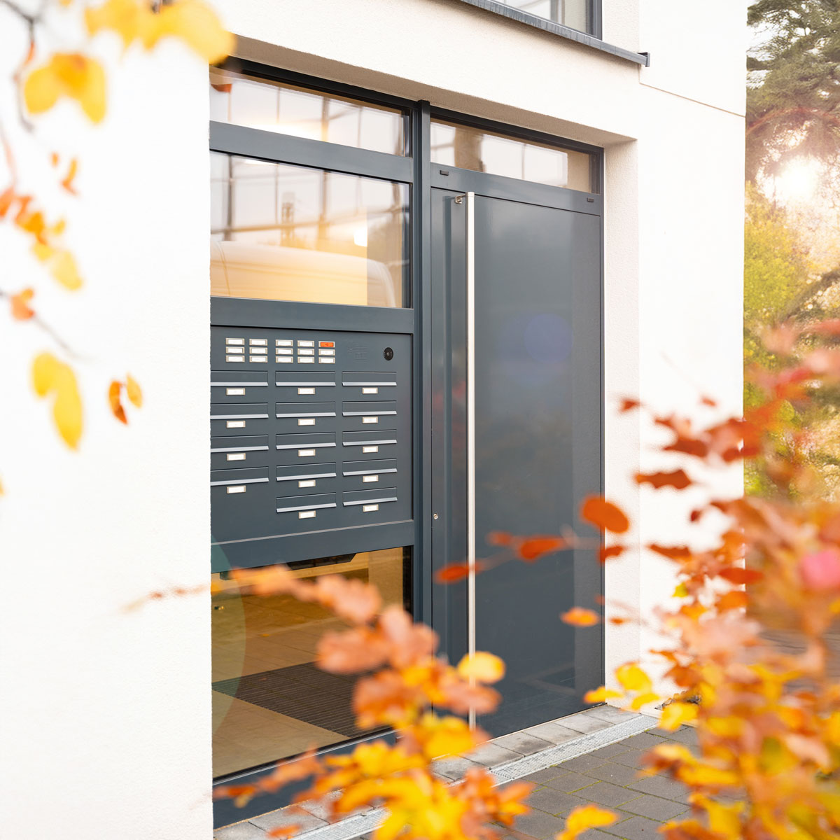 Moderner Hauseingang mit anthrazitfarbener Tuer und Briefkastenanlage im Herbst
