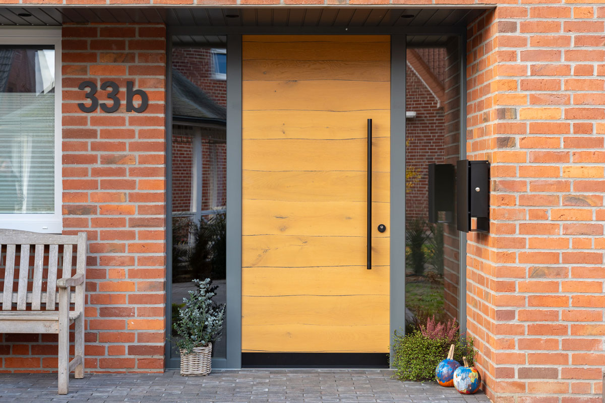 Moderne Holzhaustuer in Backsteinfassade mit Hausnummer 33b und Holzbank