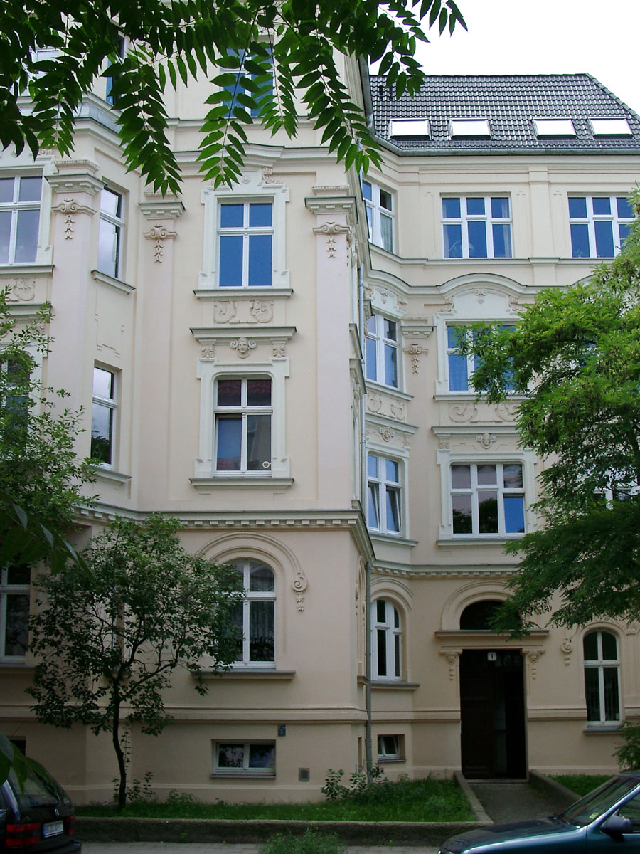 Cremefarbenes Altbaugebaeude mit Stuckfassade und Baeumen davor