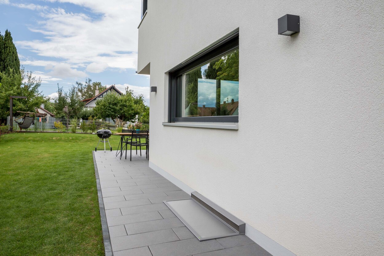 Moderne weisse Hausfassade mit Terrasse Grill und gepflegtem Garten im Sommer